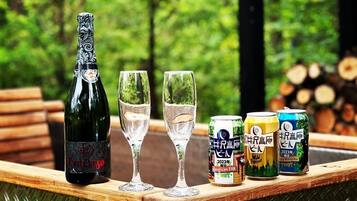 A bottle of wine, two glasses, and three cans of beer on a wooden table with a forest background.
