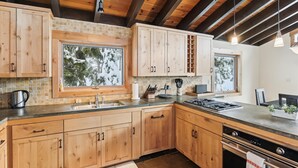 Une cuisine moderne avec des meubles en bois, un four encastré et une grande fenêtre donnant sur des arbres couverts de neige.