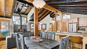 L’intérieur d’un chalet rustique, avec une cheminée en pierre, une table à manger en bois et un coin cuisine.