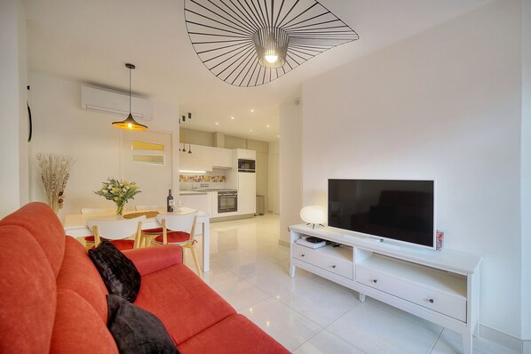 A modern living room with a red sofa, a TV on a white stand, and a kitchen in the background. - 2 PIECES MODERNE  300 m plages Croisette A1B238 (Cannes)