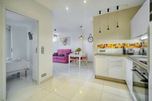 A modern kitchen with white cabinets, a dining area with a pink sofa, and a bed in the adjacent room. - 2 PIECES MODERNE  300 m plages Croisette A1B238 (Cannes)