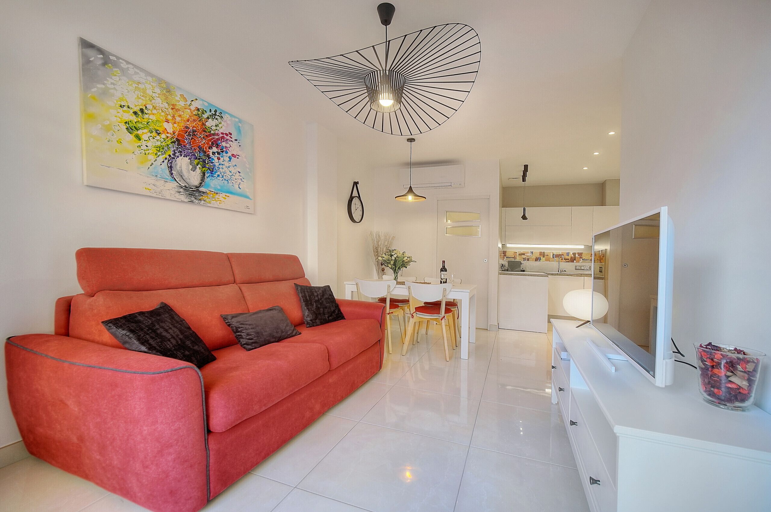 A modern living room with a red sofa, a dining area, and a kitchen in the background.