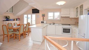 A kitchen with white cabinets, a microwave, an oven, and a dining area with a table and chairs.