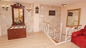 A room with a wooden cabinet, a large mirror, a red sofa, a staircase with a white railing, and stone walls.