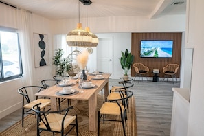 Uma área de refeições com mesa de madeira, cadeiras pretas e luminária pendente trançada.