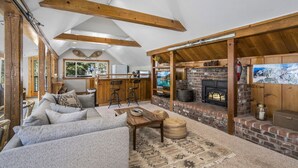 A cozy living room with a sofa, a coffee table, and a fireplace. There is a kitchen area with a counter and bar stools. - Rivendell - Escape at Historic Home in Olympic Valley, Near Village, Golf, and Minutes to Tahoe (Olympic Valley)