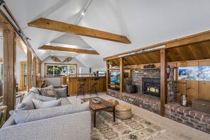 A cozy living room with a sofa, a coffee table, and a fireplace. There is a kitchen area with a counter and bar stools.