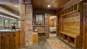 A rustic cabin interior with exposed wooden beams, a stone fireplace, a wooden bench, and a stone-tiled floor. - Rivendell - Escape at Historic Home in Olympic Valley, Near Village, Golf, and Minutes to Tahoe (Olympic Valley)
