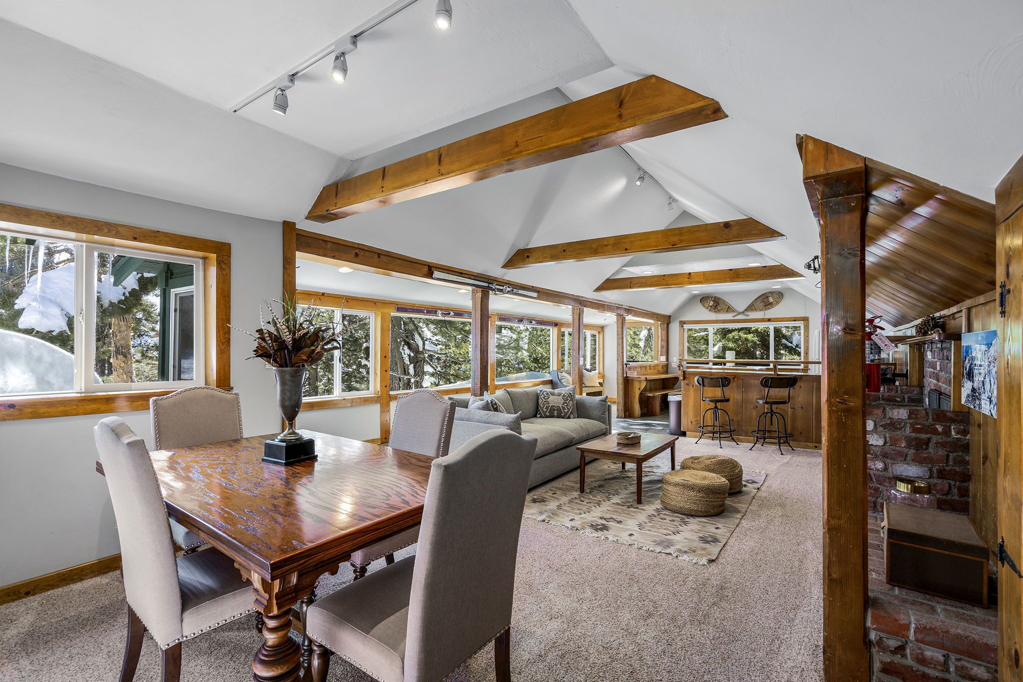 A spacious living area with a wooden dining table, comfortable seating, and large windows offering views of the outdoors.