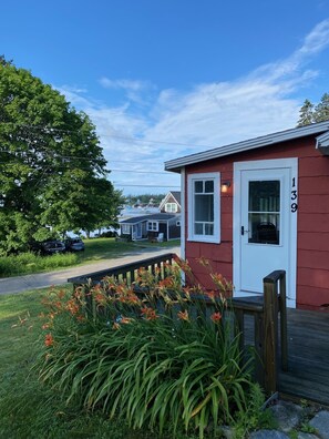 Un bâtiment rouge avec une porte blanche portant le numéro « 139 » et un petit porche agrémenté de fleurs et de plantes.