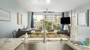 A modern kitchen with a sink, a dining area with a table and chairs, a sofa, and a television.