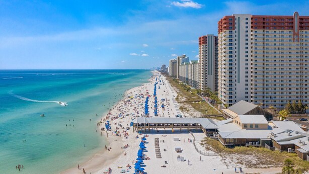 A beachside hotel with a long beachfront, multiple floors, and a covered area with umbrellas.