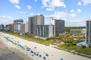 Et strandhotel med flere høje bygninger, en sandstrand med parasoller og et poolområde.