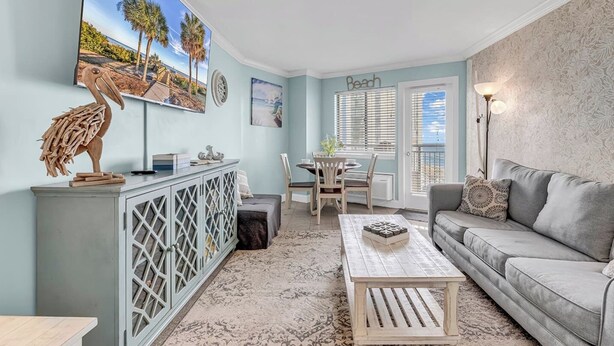 A living room with a sofa, a coffee table, a dining area with a table and chairs, a cabinet with a decorative item, and a wall with a beach-themed painting.