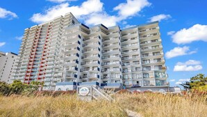 Een hotel met meerdere verdiepingen, balkons, een zandpad ervoor en een helderblauwe lucht.