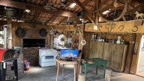 A rustic kitchen with a brick oven, wooden beams, and a television displaying a cooking show. - Haras Trevo de Ferro (Torres)