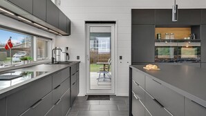 A modern kitchen with a large island, built-in appliances, and a view through a glass door. - 2 bedroom cozy home in Juelsminde (Juelsminde)