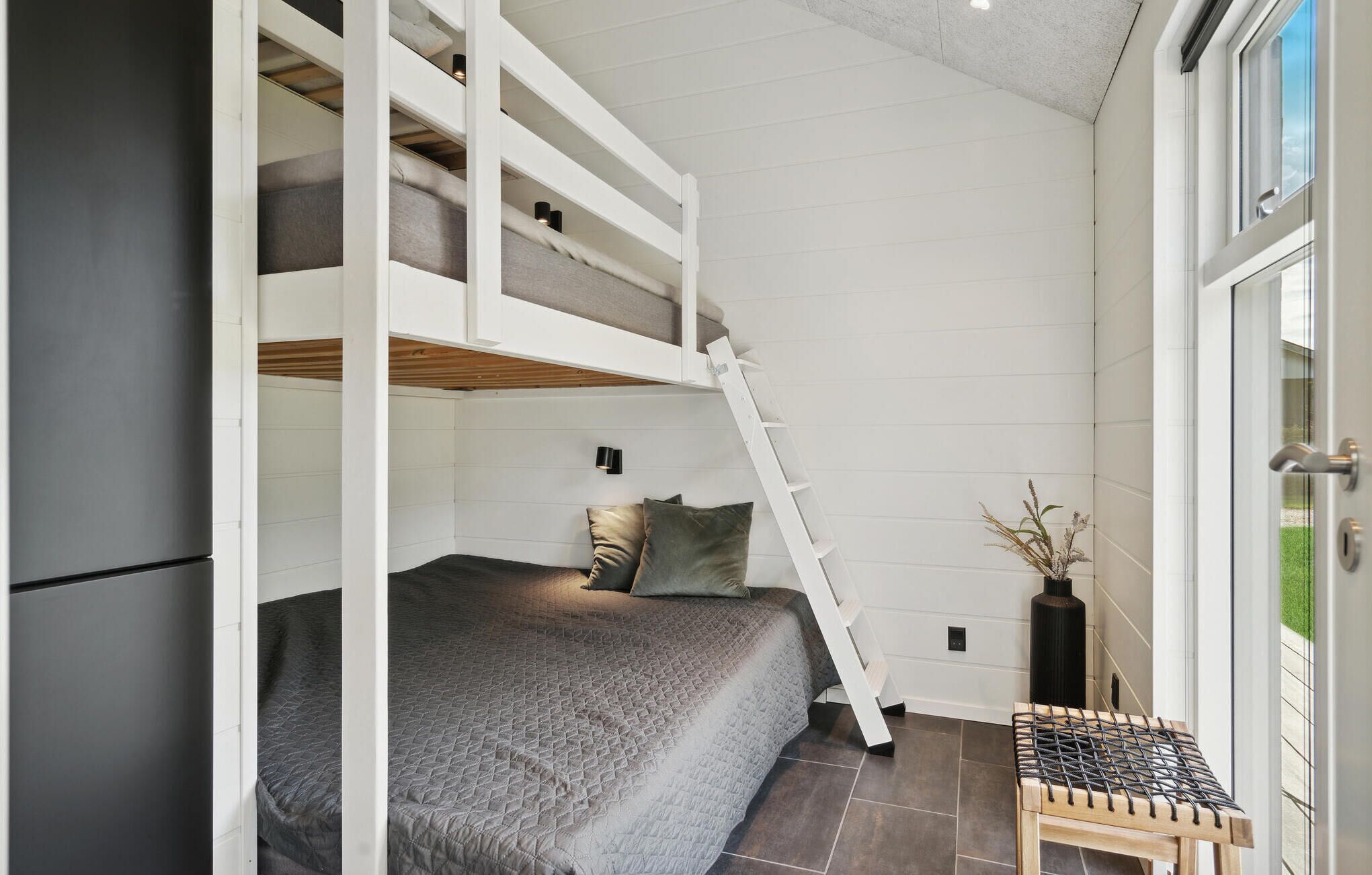 Een kleine kamer met een stapelbed, een tafeltje en een ladder.