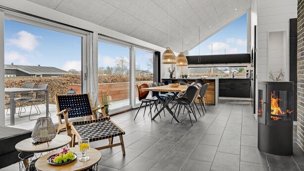 A modern kitchen with a large island, a dining area with a wooden table and chairs, and a fireplace. - 2 bedroom cozy home in Juelsminde (Juelsminde)