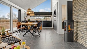 A modern kitchen with a large island, black cabinets, and a fireplace. - 2 bedroom cozy home in Juelsminde (Juelsminde)