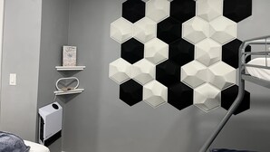 Una habitación con una cama litera, un calentador de pared, un estante con un cuadro enmarcado y un adorno geométrico en la pared.