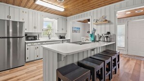Une cuisine moderne avec des meubles blancs, un réfrigérateur en acier inoxydable, un four à micro-ondes encastré et un grand îlot central doté de tabourets de bar.