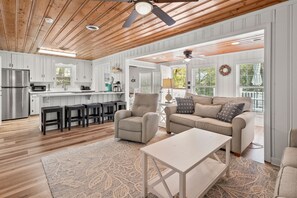 A spacious living area with a sofa, armchair, and coffee table, a kitchen with white cabinets and a stainless steel refrigerator, and a ceiling fan. - Cozy, pet-friendly home - blocks from the ocean - close to shops, eateries, entertainment (North Myrtle Beach)