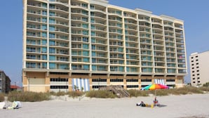 Een meerhoog hotel met balkons, een ligging aan het strand en een kleurrijke parasol.