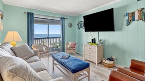 Ett vardagsrum med en soffa, fåtöljer, ett soffbord, en tv och utsikt över havet.