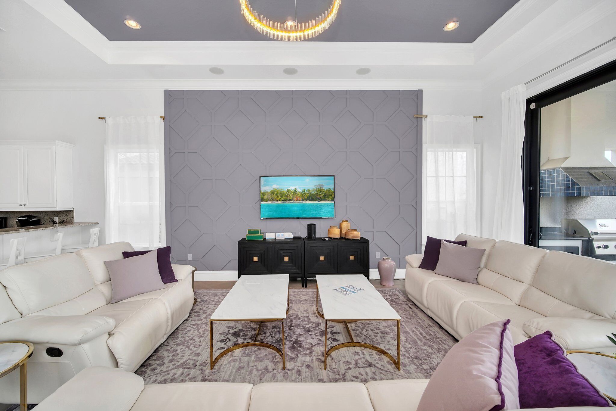 Een moderne woonkamer met een zithoek, twee salontafels, een televisie en een keukenruimte zichtbaar door een open deur.