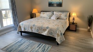 Un dormitorio con una cama, dos lámparas de noche, un cuadro y una ventana con cortinas.