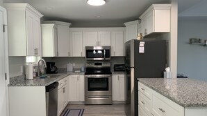 Una cocina moderna con armarios blancos, electrodomésticos de acero inoxidable, encimeras de granito y una alfombra azul.