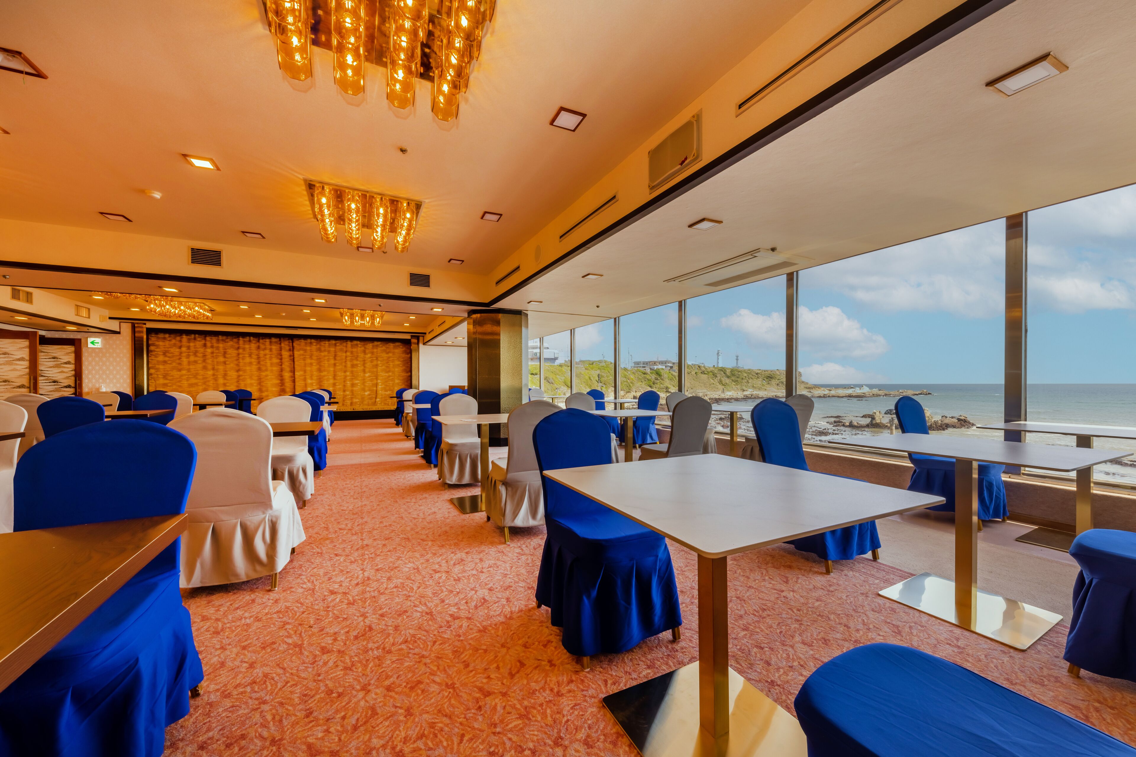 Une salle de conférence équipée de tables et de chaises, de grandes fenêtres donnant sur la plage et d’un lustre.
