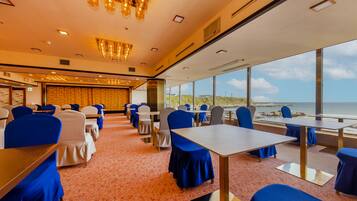 A conference room with tables and chairs, large windows with a view of the beach, and a chandelier.
