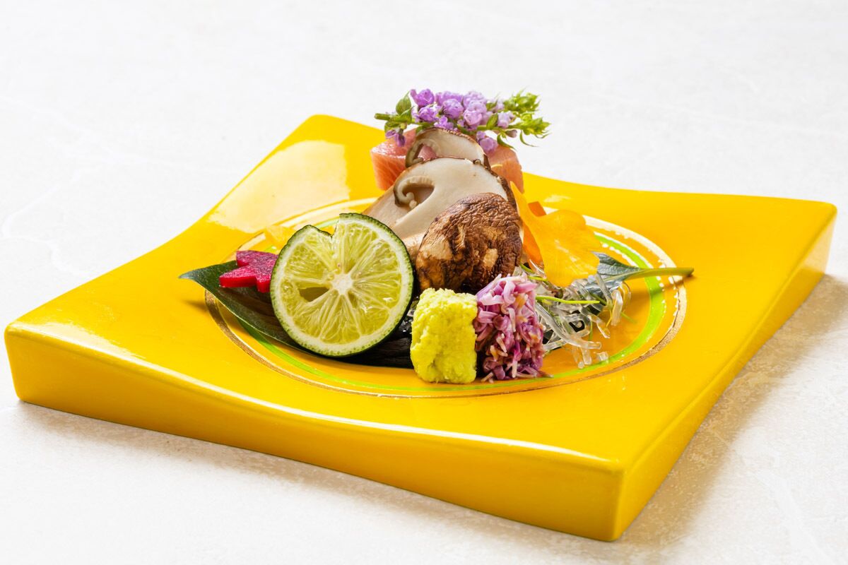 A yellow plate with a slice of meat, lime, and red onions.