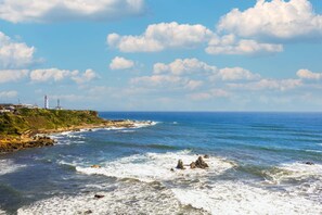 A coastal landscape with rocky shores, a lighthouse, and a clear blue sky.