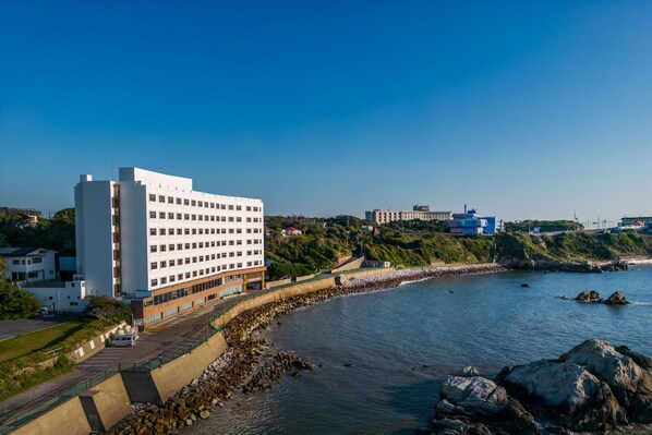 A coastal hotel with a modern design, featuring a prominent white building with multiple floors and a parking area adjacent to the beach.