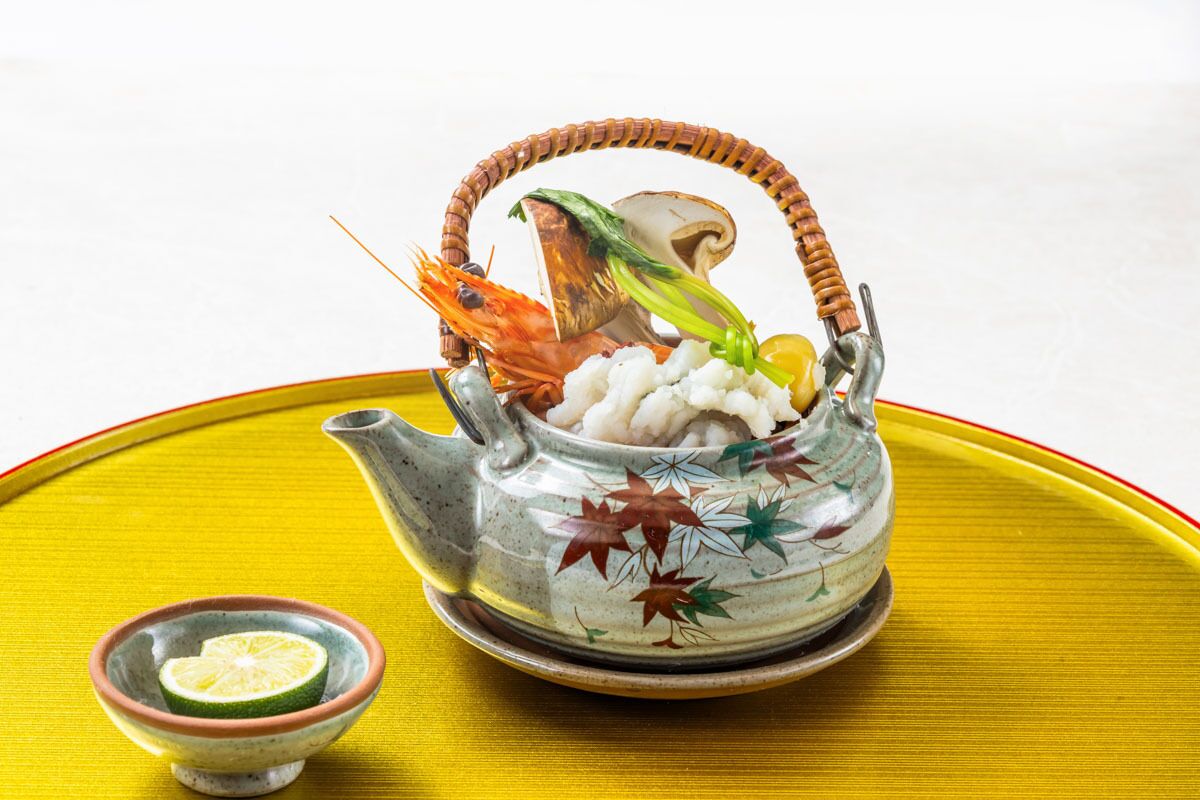 A teapot with a floral design, a bowl of lime, and a basket containing a shrimp and a mushroom.