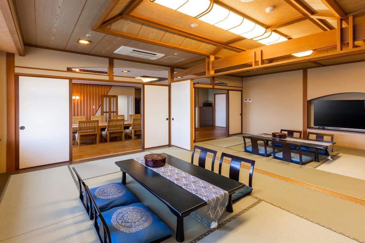 A traditional Japanese room with tatami flooring, a low table with cushions, and a television.