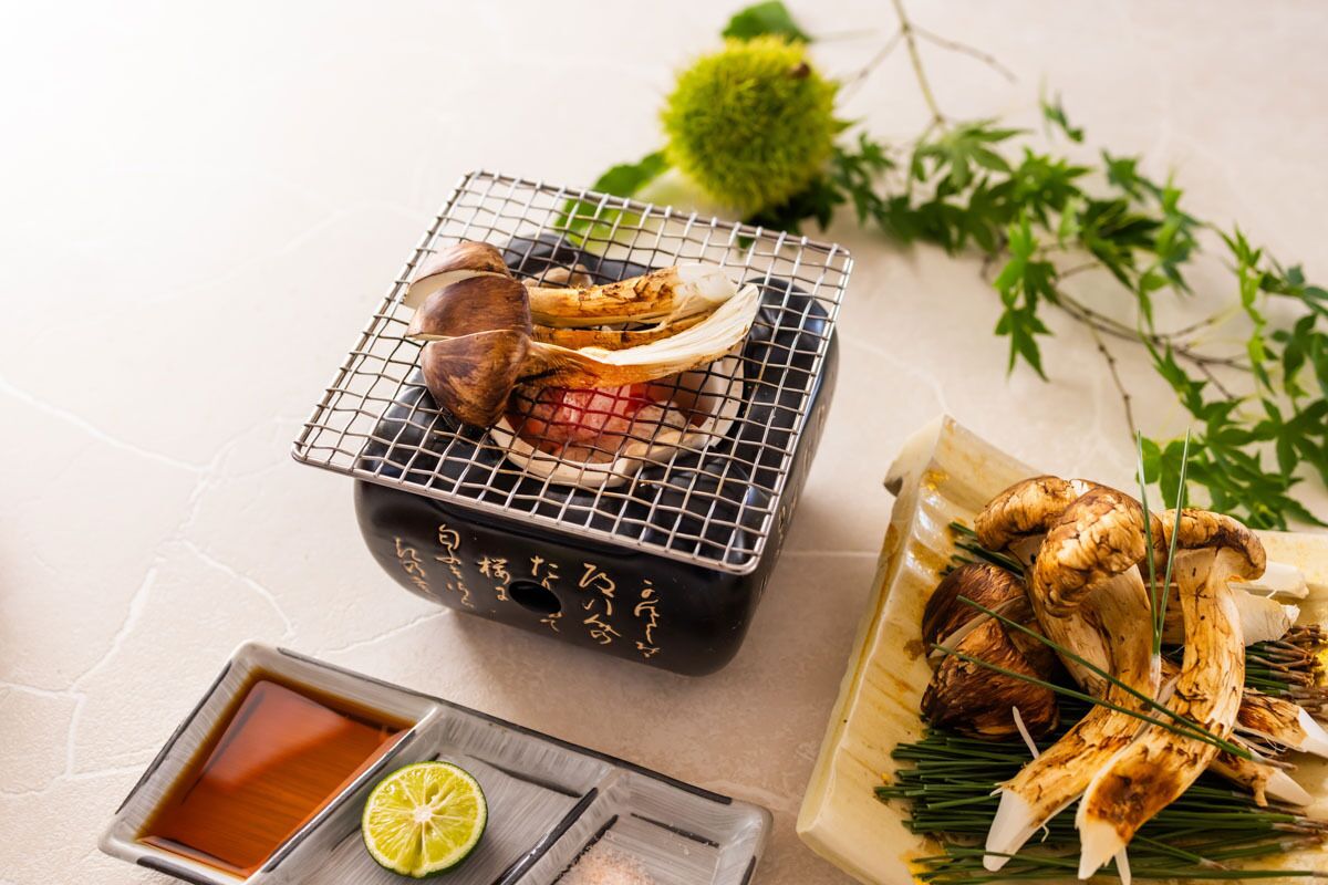 Uma bancada de cozinha com uma grelha, um recipiente com molho e um prato de cogumelos.