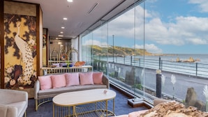 Une chambre moderne dotée d’une grande fenêtre donnant sur la côte, d’un canapé, d’une petite table et d’une fresque murale décorative.