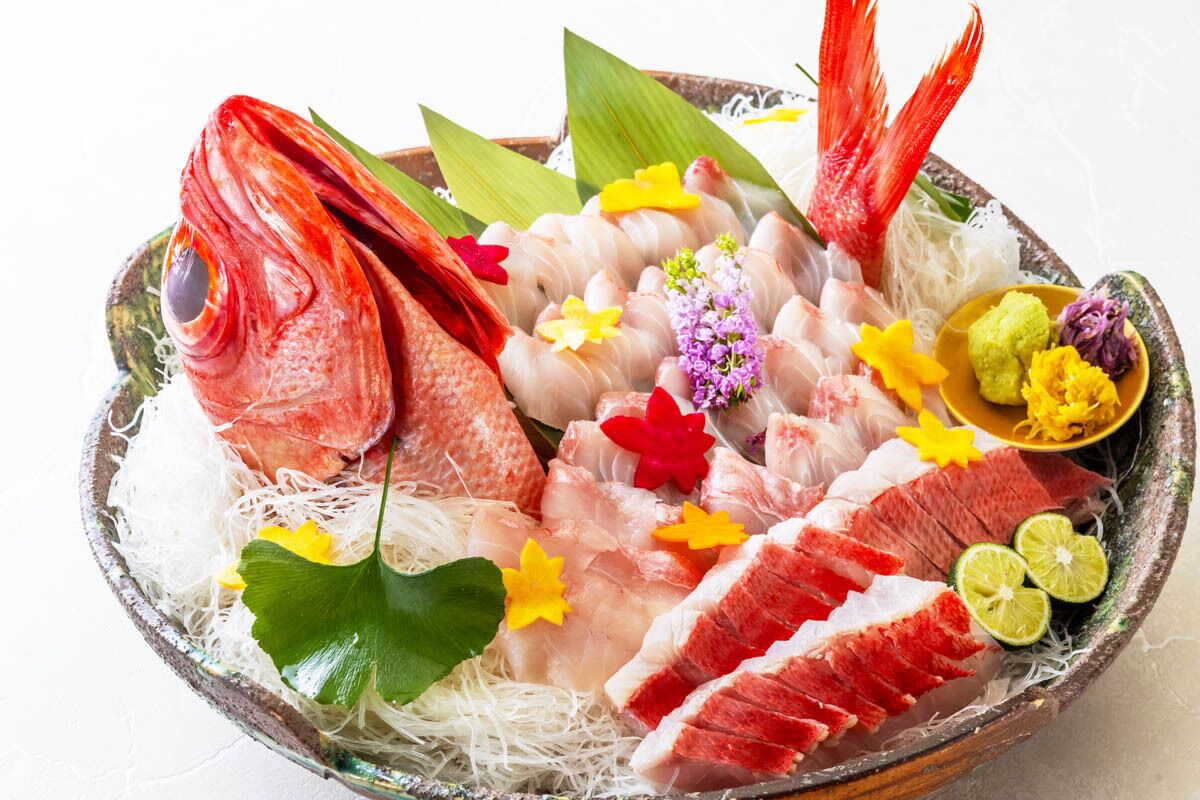 Variedad de mariscos frescos, como pescado, camarones y langosta, presentados sobre hielo con flores y hojas decorativas.