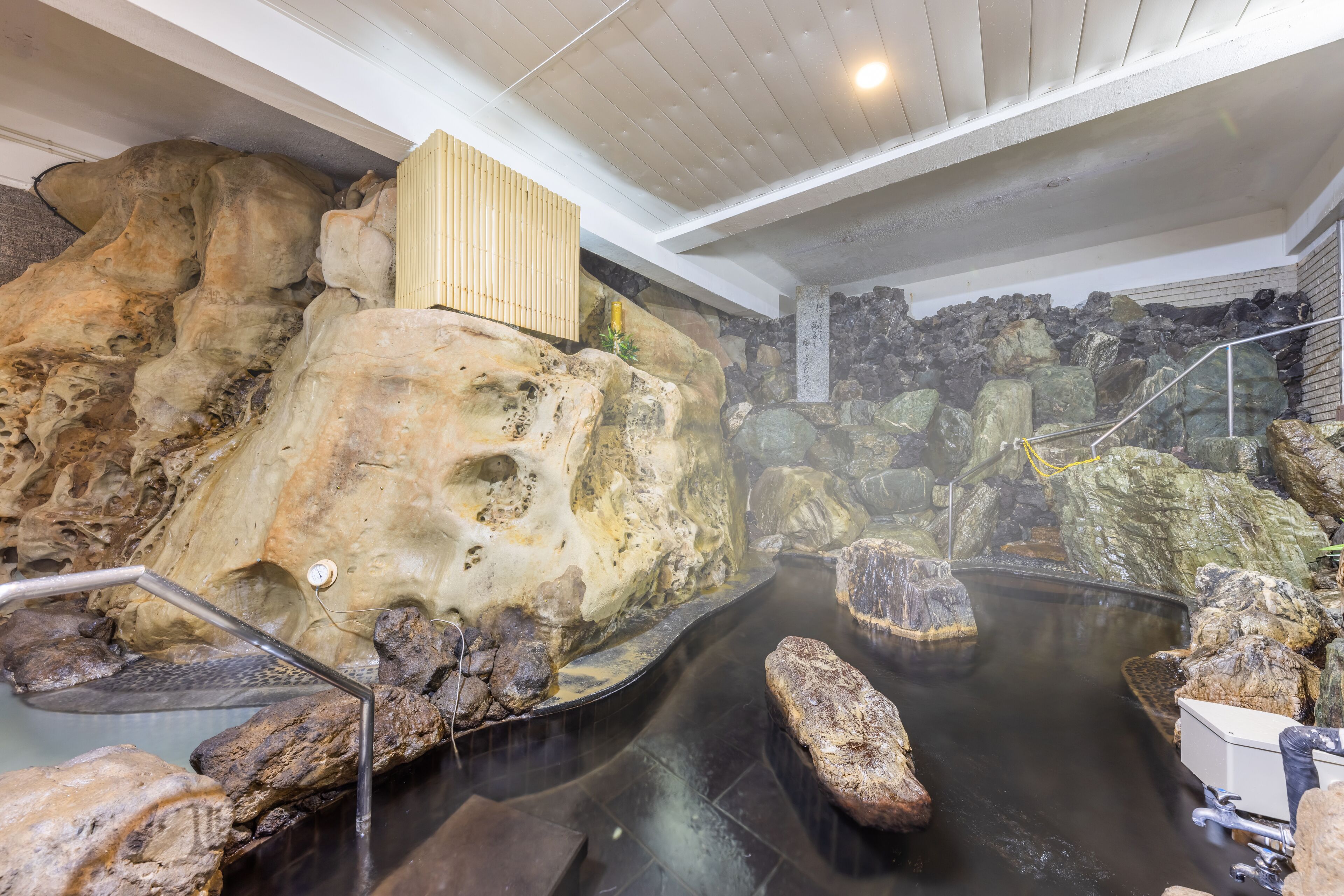 Un área de aguas termales con grandes rocas, un banco de madera y un muro de piedra.
