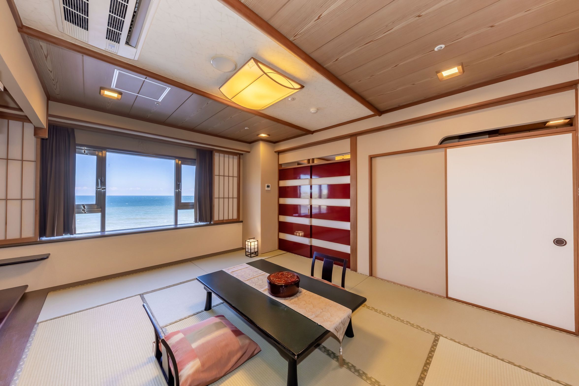 A traditional Japanese room with tatami flooring, a low table with a cushion, a view of the sea, and sliding doors.
