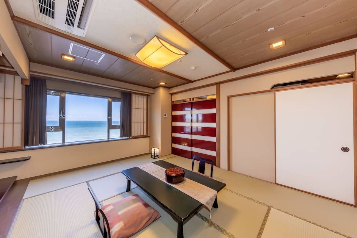 A traditional Japanese room with tatami flooring, a low table with a cushion, a view of the sea, and sliding doors.