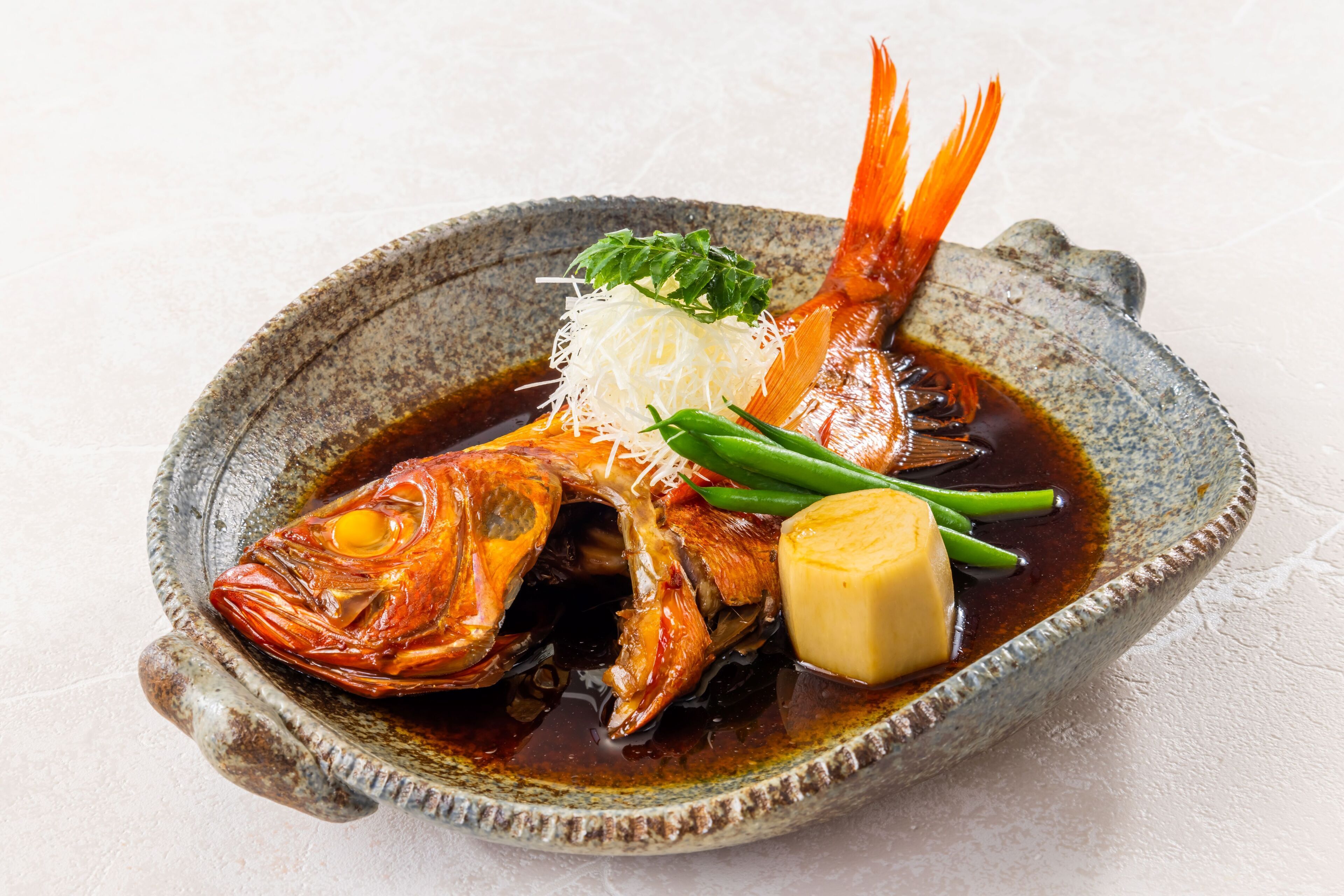 A bowl of food with a fish, vegetables, and a piece of tofu.