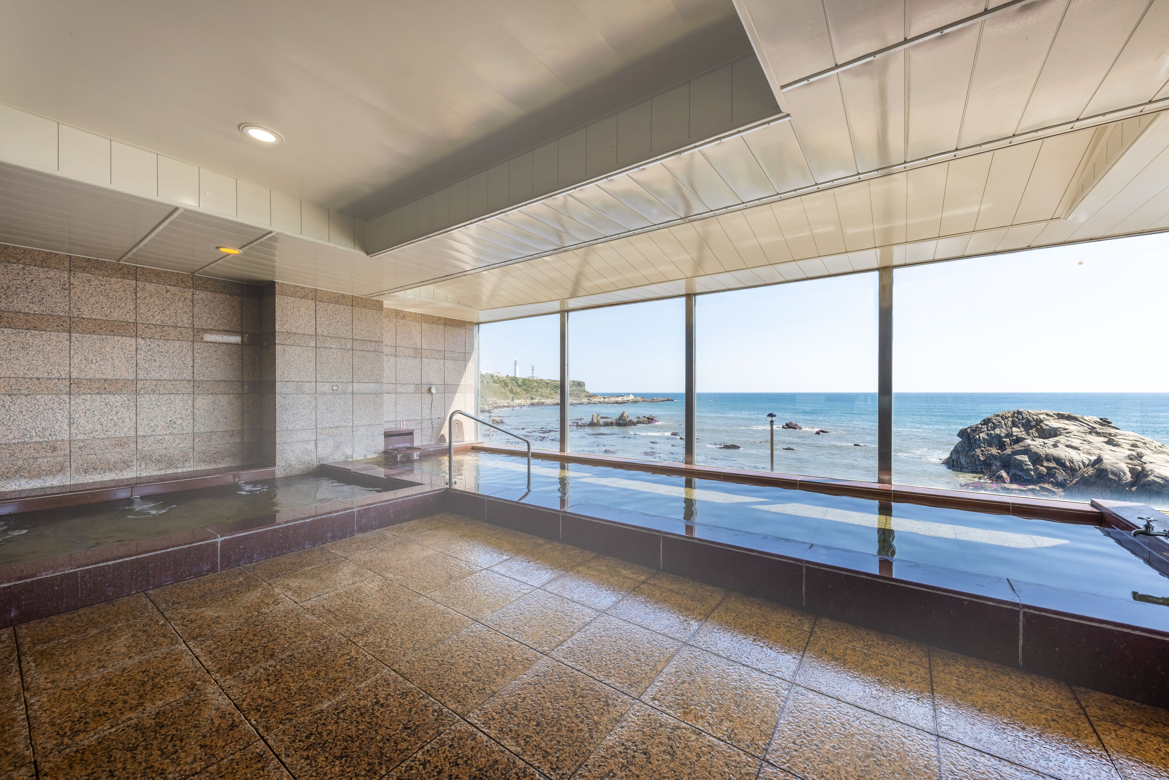 Un espace spa doté d’une grande fenêtre donnant sur la mer, d’un mur en pierre et d’un sol carrelé.