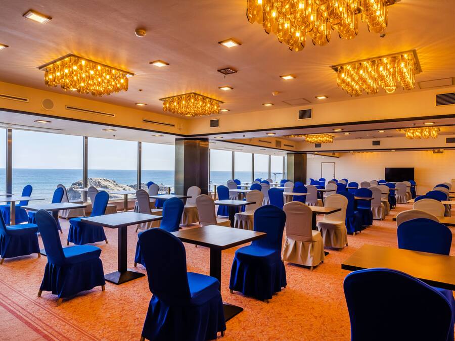 A conference room with tables and chairs, large windows with a view of the ocean, and chandeliers.