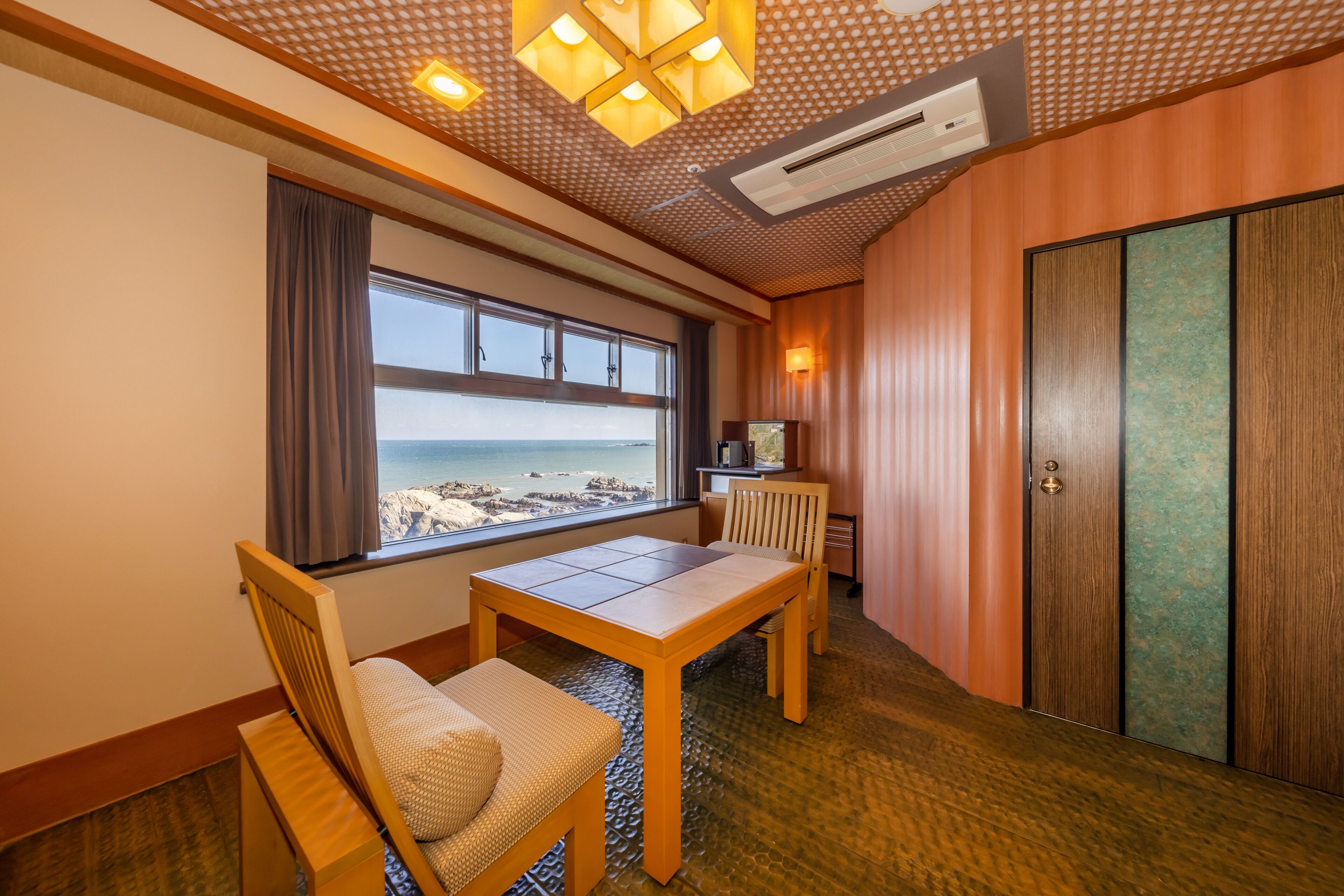 A room with a wooden table and chairs, a large window with a view of the sea, and a sliding door.