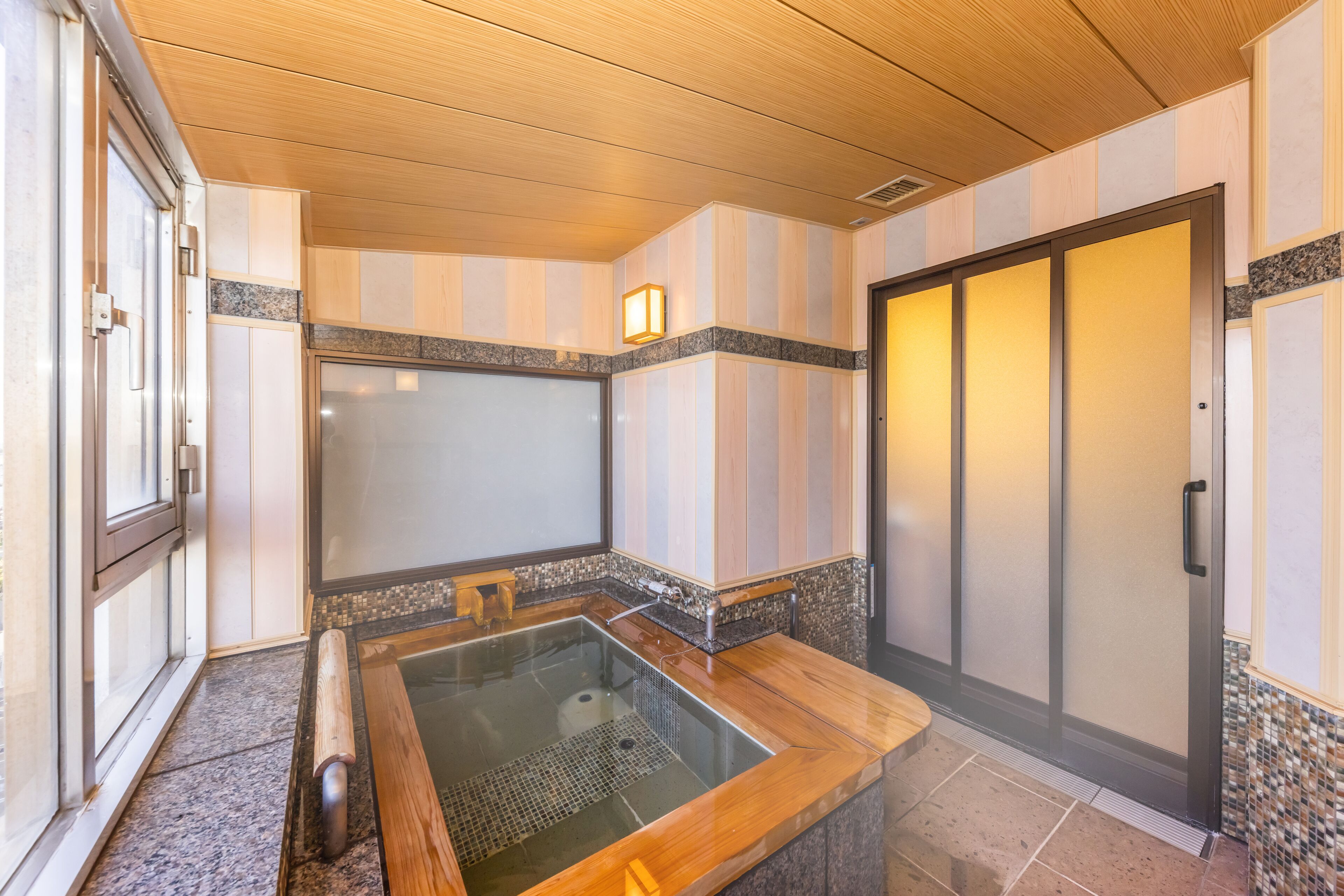 A modern bathroom with a glass-enclosed hot tub, wooden flooring, and a sliding door.